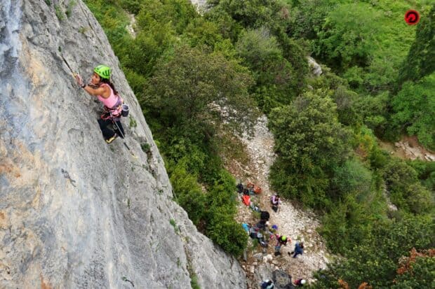 A woman is rock climbing on a steep cliff with a forest below, HD Desktop Wallpaper
