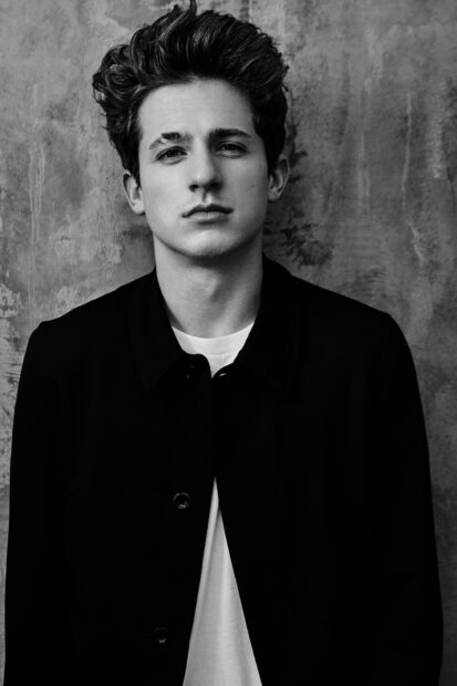 Charlie Puth stands against a textured wall wearing a black jacket and white shirt, HD Mobile Wallpaper