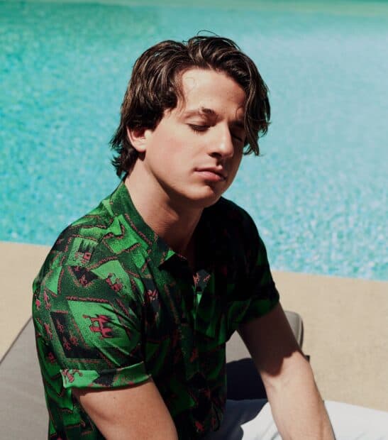 Charlie Puth is sitting with his eyes closed near a pool wearing a patterned green shirt, HD Phone Wallpaper