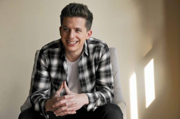Charlie Puth sitting on a chair smiling with hands clasped in a casual outfit, HD Desktop Wallpaper