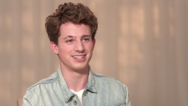 Charlie Puth smiles warmly wearing a light denim jacket during an interview, HD Desktop Wallpaper