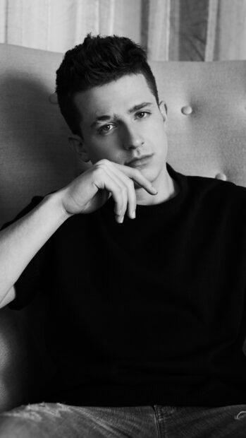 Charlie Puth is sitting on a chair with his hand near his face in a black and white photo, 4K Phone Wallpaper