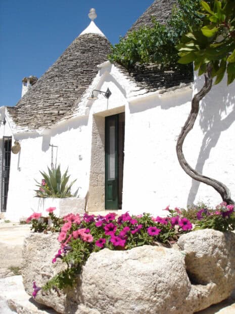 A traditional Alberobello house with stone roof and vibrant flowers under a clear blue sky, HD Mobile Wallpaper