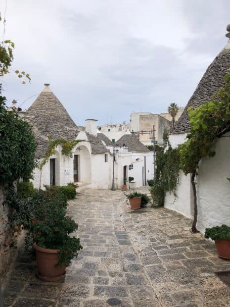 A narrow stone street with traditional Alberobello houses and greenery, HD Desktop Wallpaper