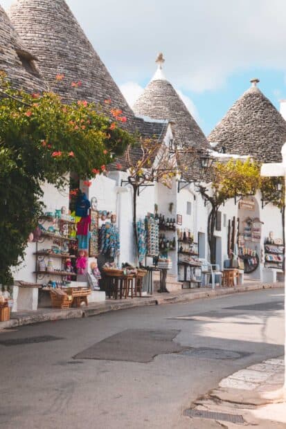 This image shows a peaceful street with traditional stone roofs and shops in Alberobello, 2K Mobile Wallpaper