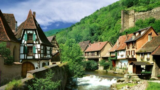 A peaceful village with traditional houses and flowing river surrounded by green hills is shown in this Village Wallpapers, HD Desktop Wallpaper