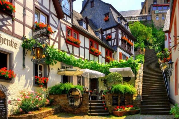 A charming village scene shows traditional houses decorated with vibrant flowers near stone stairs, HD Desktop Wallpaper