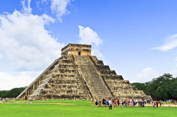 A large group visiting the ancient Chichen Itza pyramid under a partly cloudy blue sky, 2K Desktop Wallpaper