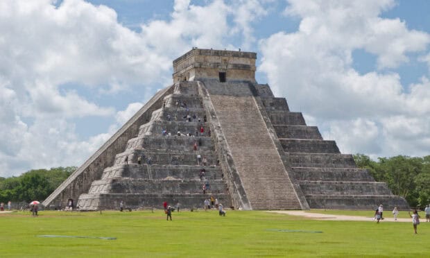 The Chichen Itza pyramid stands under a blue sky with visitors exploring the historic site, 2K Desktop Wallpaper