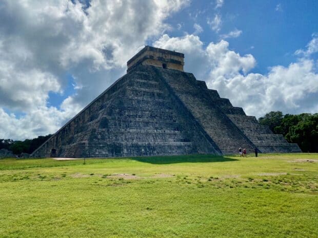 The Chichen Itza ancient pyramid stands under a partly cloudy sky with green grass around, 2K Desktop Wallpaper