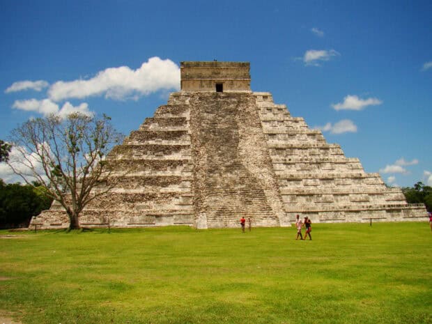 The Chichen Itza pyramid stands tall under blue sky with green grass and visitors, HD Desktop Wallpaper