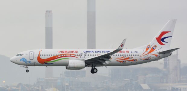 A China Eastern Airlines plane flies near an industrial area during landing preparation, 2K Desktop Wallpaper