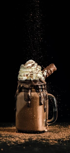 Cocoa powder sprinkles on a chocolate milkshake topped with whipped cream and a chocolate bar, 2K Phone Wallpaper