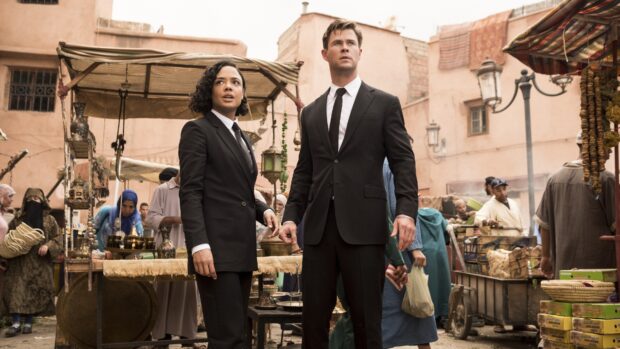 Chris Hemsworth and Tessa Thompson stand alert in a busy marketplace scene from Men In Black, 4K Desktop Wallpaper
