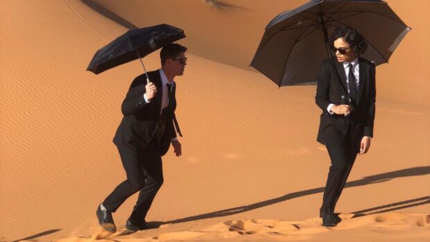Chris Hemsworth Men In Black Wallpapers shows two agents walking on sand dunes with umbrellas, HD Desktop Wallpaper