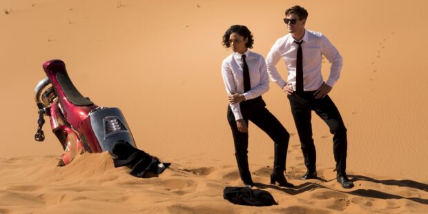 Chris Hemsworth and Tessa Thompson stand in a desert near a buried motorcycle in Men in Black, 2K Desktop Wallpaper