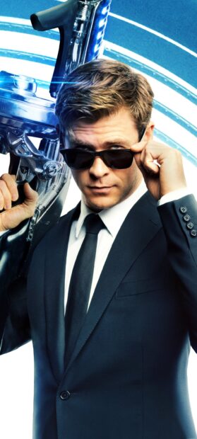 Chris Hemsworth adjusts his sunglasses while holding a futuristic weapon in a sci fi setting, 2K Phone Wallpaper