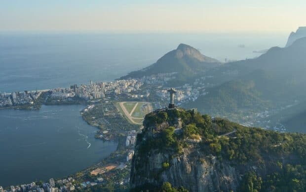 The Christ the Redeemer statue stands tall over Rio de Janeiro cityscape with mountains and ocean, 2K Desktop Wallpaper
