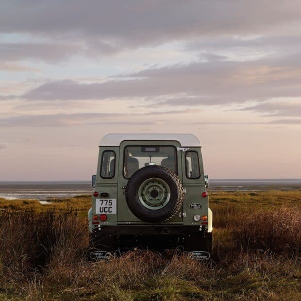 A Land Rover Defender is parked on grassy land near water under a cloudy sky, HD Desktop Wallpaper