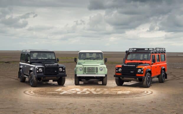 Three Land Rover Defender vehicles are parked on a sandy beach under cloudy skies, 2K Desktop Wallpaper