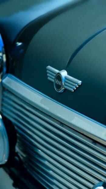 A close up of a vintage Mini Cooper emblem on the car grille with blue paint, HD Mobile Wallpaper