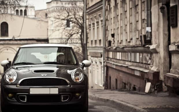 A black Mini Cooper parked on a narrow city street surrounded by old buildings, HD Desktop Wallpaper