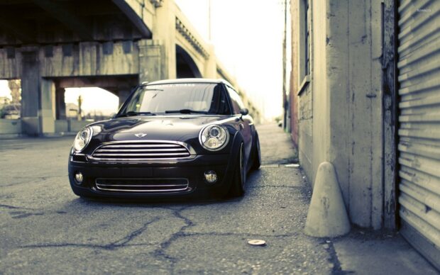 A black Mini Cooper is parked on an empty city street near buildings and an overpass, HD Desktop Wallpaper