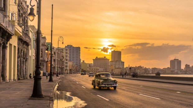 A classic car drives down a street in Havana Cuba during a golden sunset, HD Desktop Wallpaper