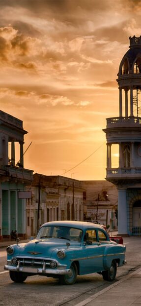 A classic blue car parked on a street with historic buildings during sunset in Havana Cuba, 2K Mobile Wallpaper