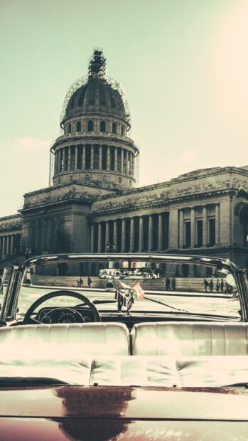A classic car is parked with a view of Havana Cuba cityscape and a historic building, HD Mobile Wallpaper