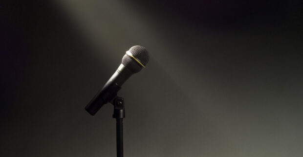 A classic microphone stands in a focused spotlight against a dark background, featuring microphone wallpapers, HD Desktop Wallpaper