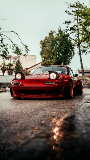 A red Mazda MX 5 Miata is parked on a wet street with its headlights on during a rainy day, HD Mobile Wallpaper