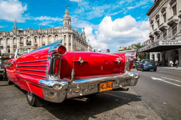 A classic red vintage car is parked on a busy street in Havana Cuba with historic buildings, 2K Desktop Wallpaper