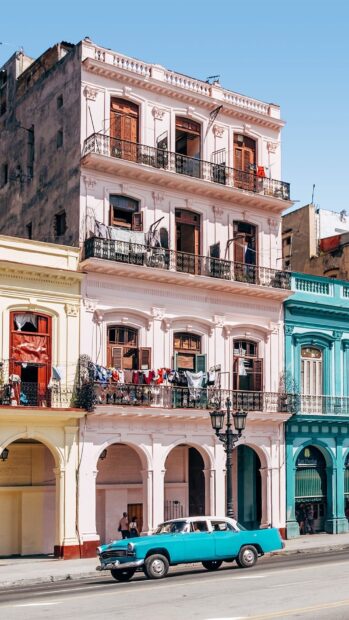 A classic vintage car is parked in front of colorful Havana Cuba buildings under a clear sky, HD Mobile Wallpaper