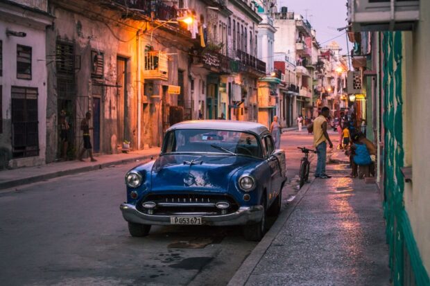 A classic vintage car is parked on a lively Havana street showcasing the city's vibrant culture and architecture, HD Desktop Wallpaper