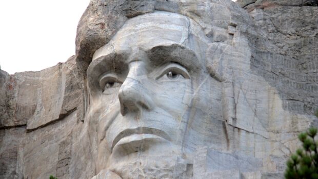 A close up view of Abraham Lincoln's carved face on Mount Rushmore shows detailed stonework, 2K Desktop Wallpaper