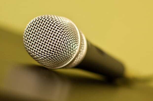 A close up view of a microphone grill with a blurred yellow background features microphone wallpapers, 2K Desktop Wallpaper