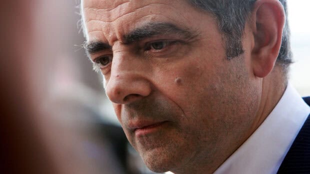 A close up image of Rowan Atkinson showing a serious expression in a formal suit, 2K Desktop Wallpaper