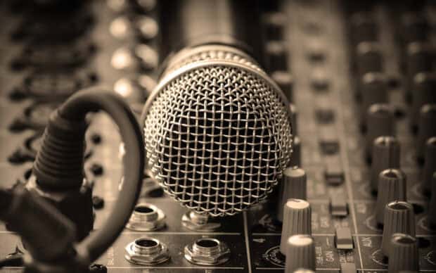 The close up image shows a microphone resting on an audio mixer with various knobs and cables, 2K Desktop Wallpaper
