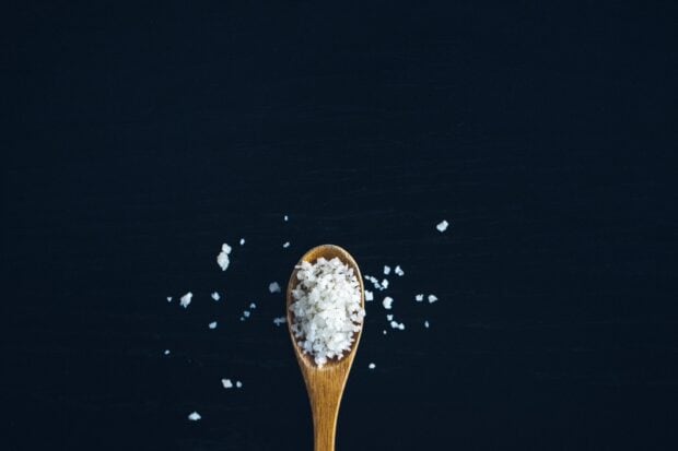 Coarse salt is shown on a wooden spoon on a dark surface with some salt grains scattered around, HD Desktop Wallpaper