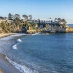 People enjoying the water at Laguna Beach with cliffs and houses nearby, 2K Desktop Wallpaper