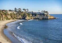 People enjoying the water at Laguna Beach with cliffs and houses nearby, 2K Desktop Wallpaper