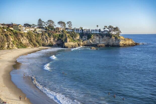 People enjoying the water at Laguna Beach with cliffs and houses nearby, 2K Desktop Wallpaper
