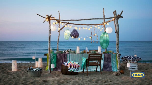 A colorful Ikea table setting is arranged on the beach with lanterns and ocean views, HD Desktop Wallpaper