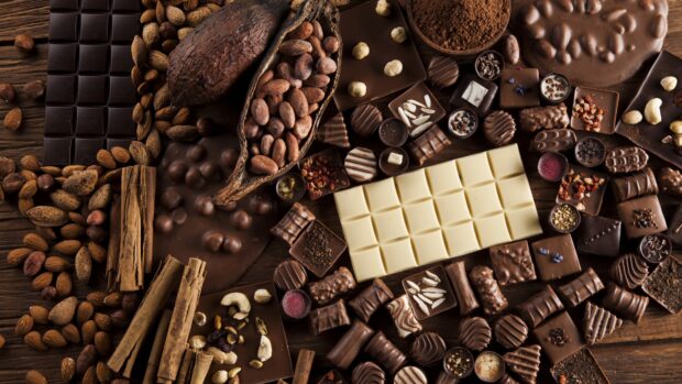 A variety of cocoa beans and assorted chocolate pieces are displayed on a wooden surface for Cocao Wallpapers, 4K Desktop Wallpaper
