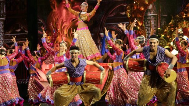 A vibrant Bollywood scene shows dancers in colorful outfits playing traditional drums on stage, HD Desktop Wallpaper