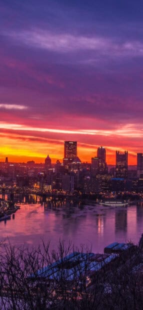 The colorful Pittsburgh skyline glows during sunset with calm river reflections and city lights, 2K Phone Wallpaper