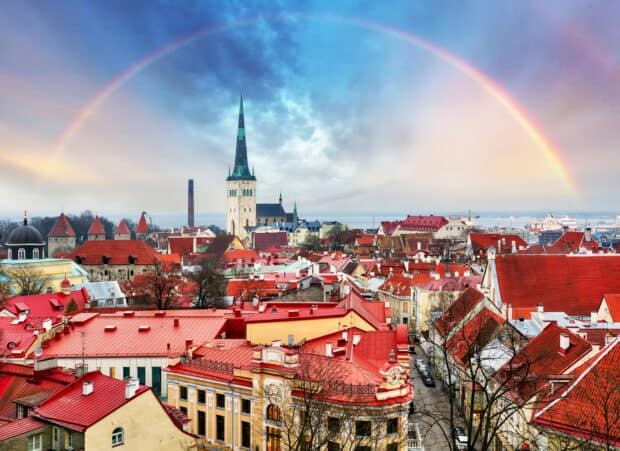 A vibrant view of Estonia's buildings with a rainbow arching across the cloudy sky, HD Desktop Wallpaper