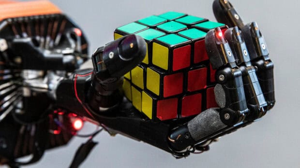 A robotic hand holds a colorful cube with red and yellow squares, 2K Desktop Wallpaper