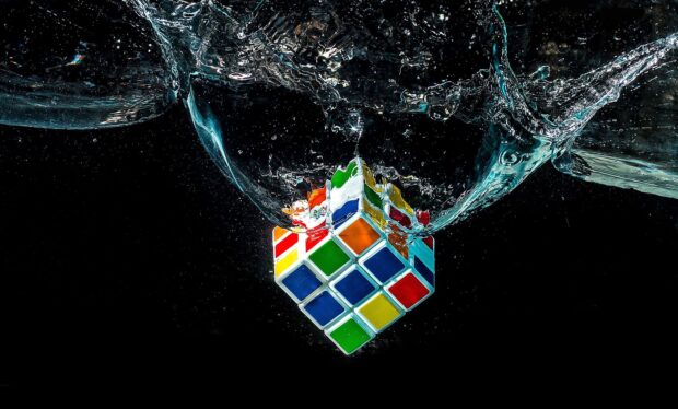 A colorful cube puzzle is splashing into water with bubbles surrounding it, HD Desktop Wallpaper